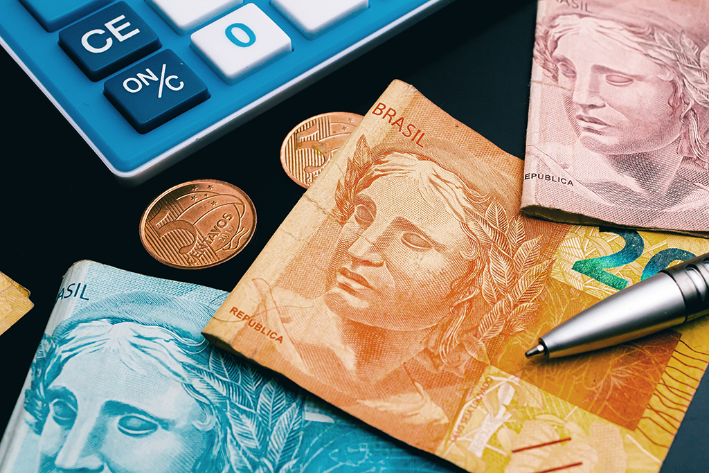 Brazilian Real banknotes on a dark wooden table with a calculator, a pen and some coins in the image composition. Concepts of Brazilian economy and finance.
